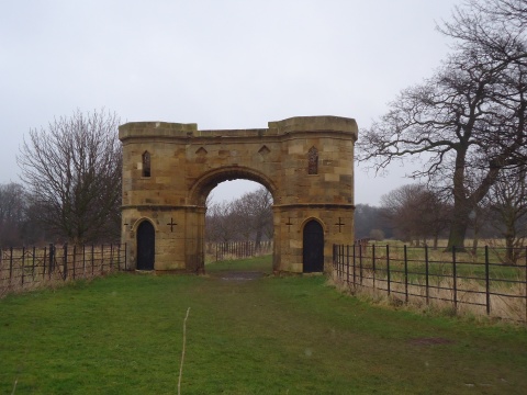 An isolated gateway between two fields is surrounded by old woodland.